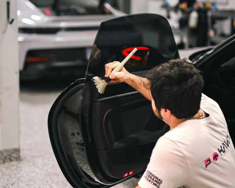Person cleaning a car door with a brush in a garage setting at element care melbourne