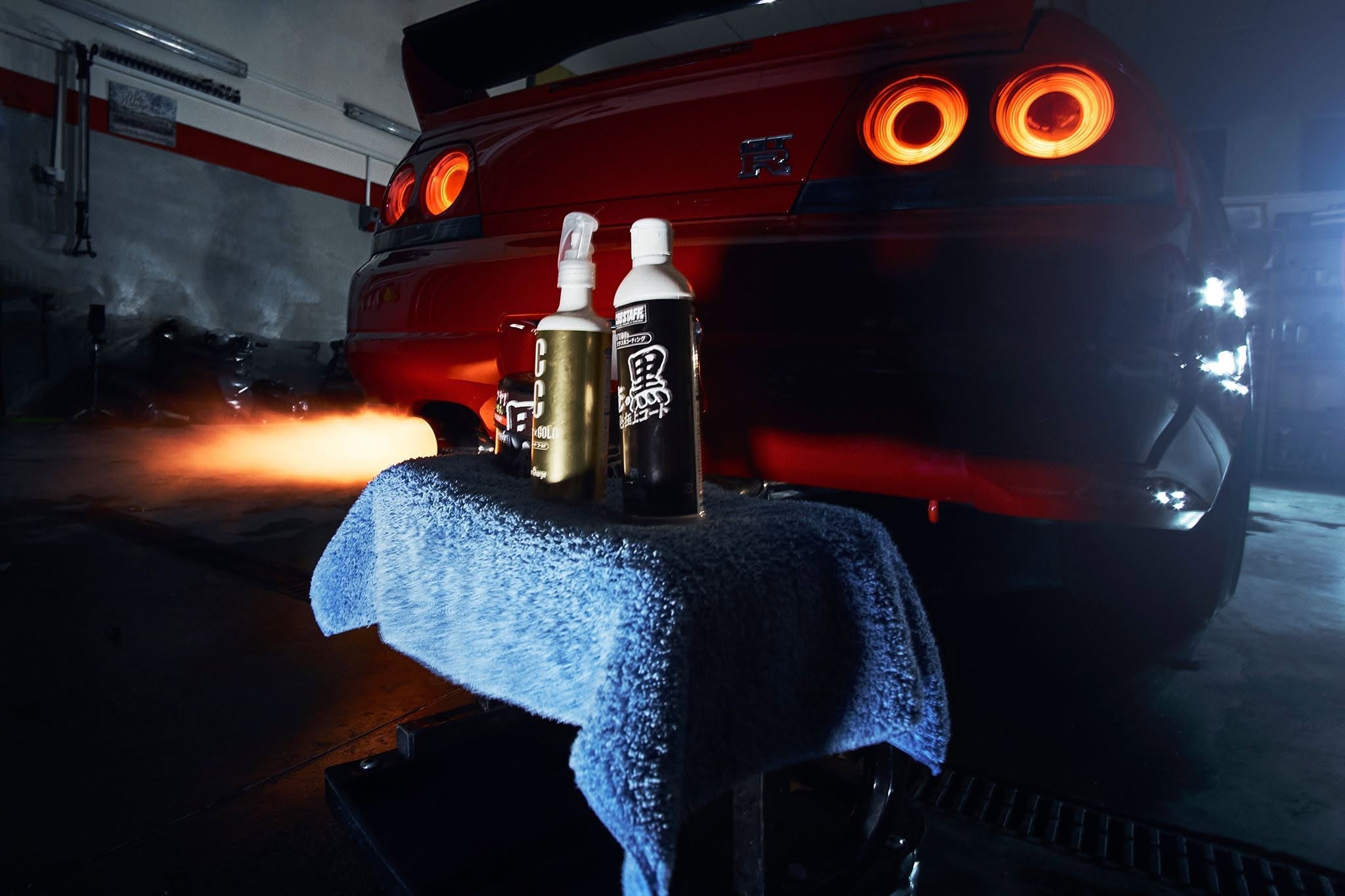 Two bottles of Prostaff car care products on a towel in front of a red car with glowing taillights.
