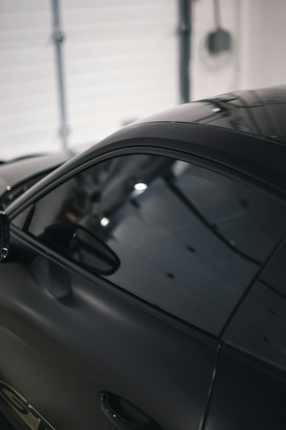 Close-up of a black car's side mirror and window highlighting window tint in a garage setting at element care melbourne